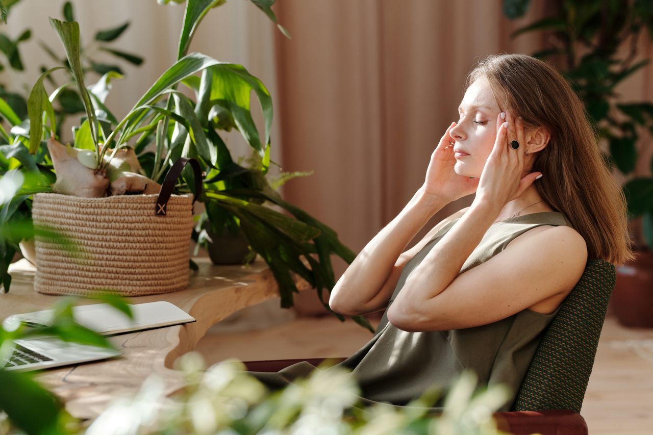 Crafting Captivating Headlines: Your awesome post title goes here A woman relaxes, massaging her temples among indoor plants in a bright, sunlit room.